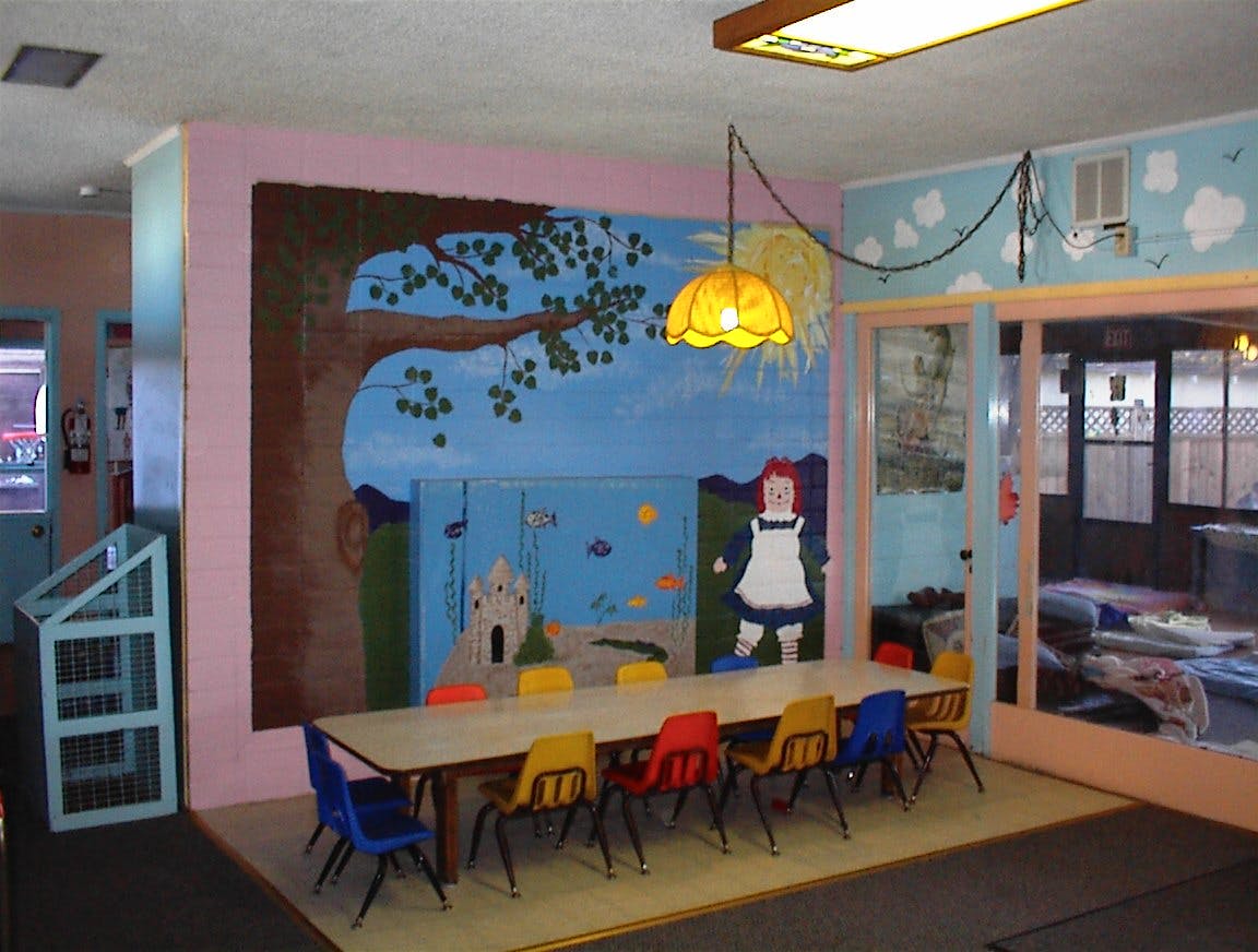 Classroom with a long table and colorful chairs, mural on the wall