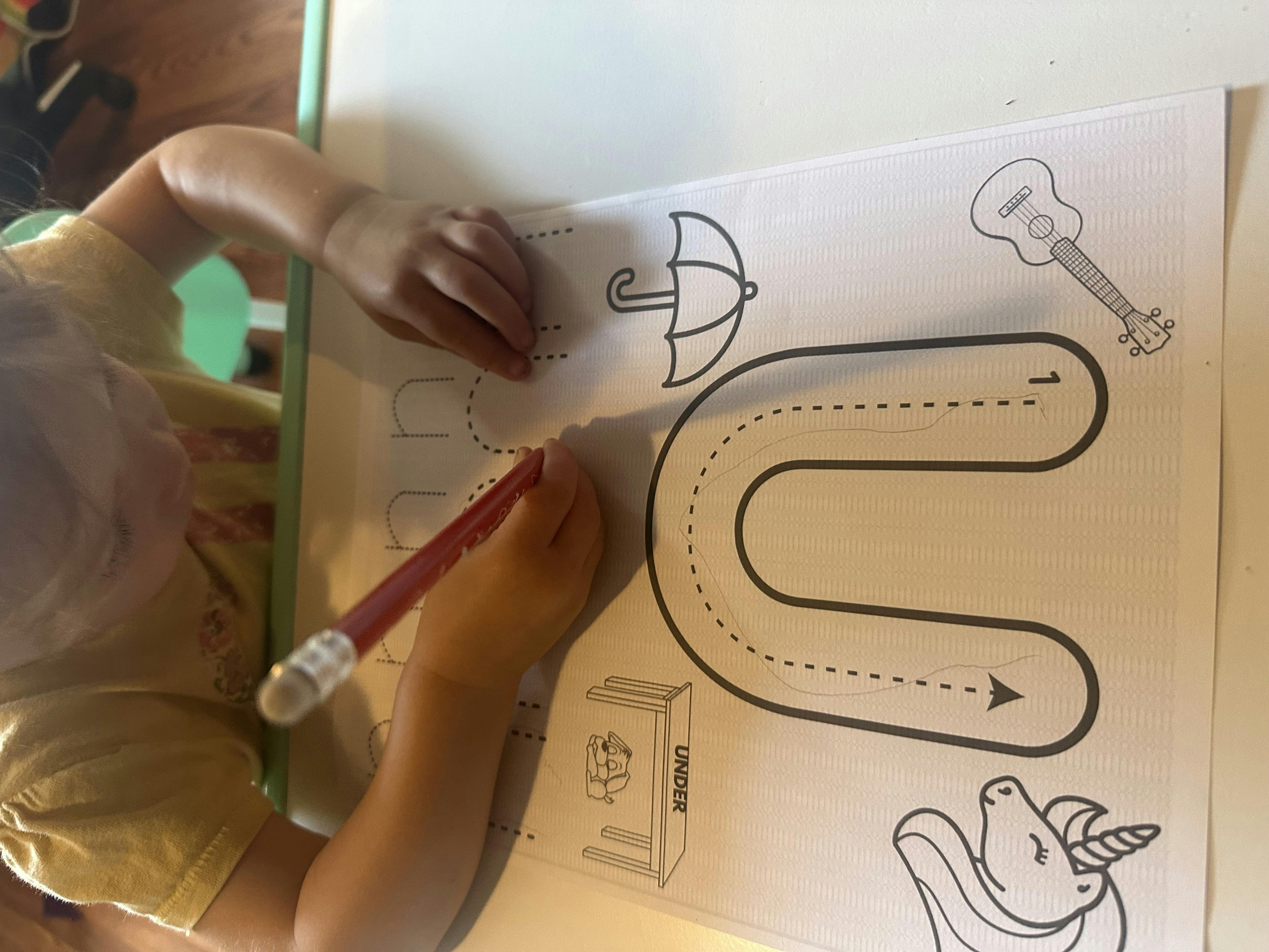Child tracing a letter U on a worksheet with a pencil