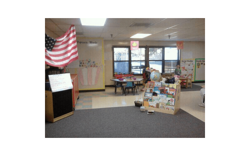 Classroom with an American flag, bulletin boards, tables, chairs, and books