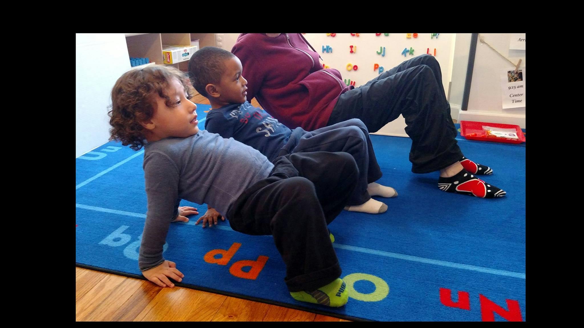 Two children and an adult sitting on a blue mat with letters