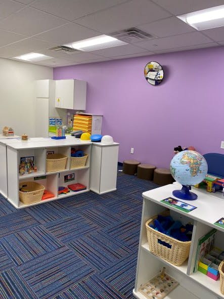 Classroom with purple wall, blue patterned carpet, and white shelves with toys
