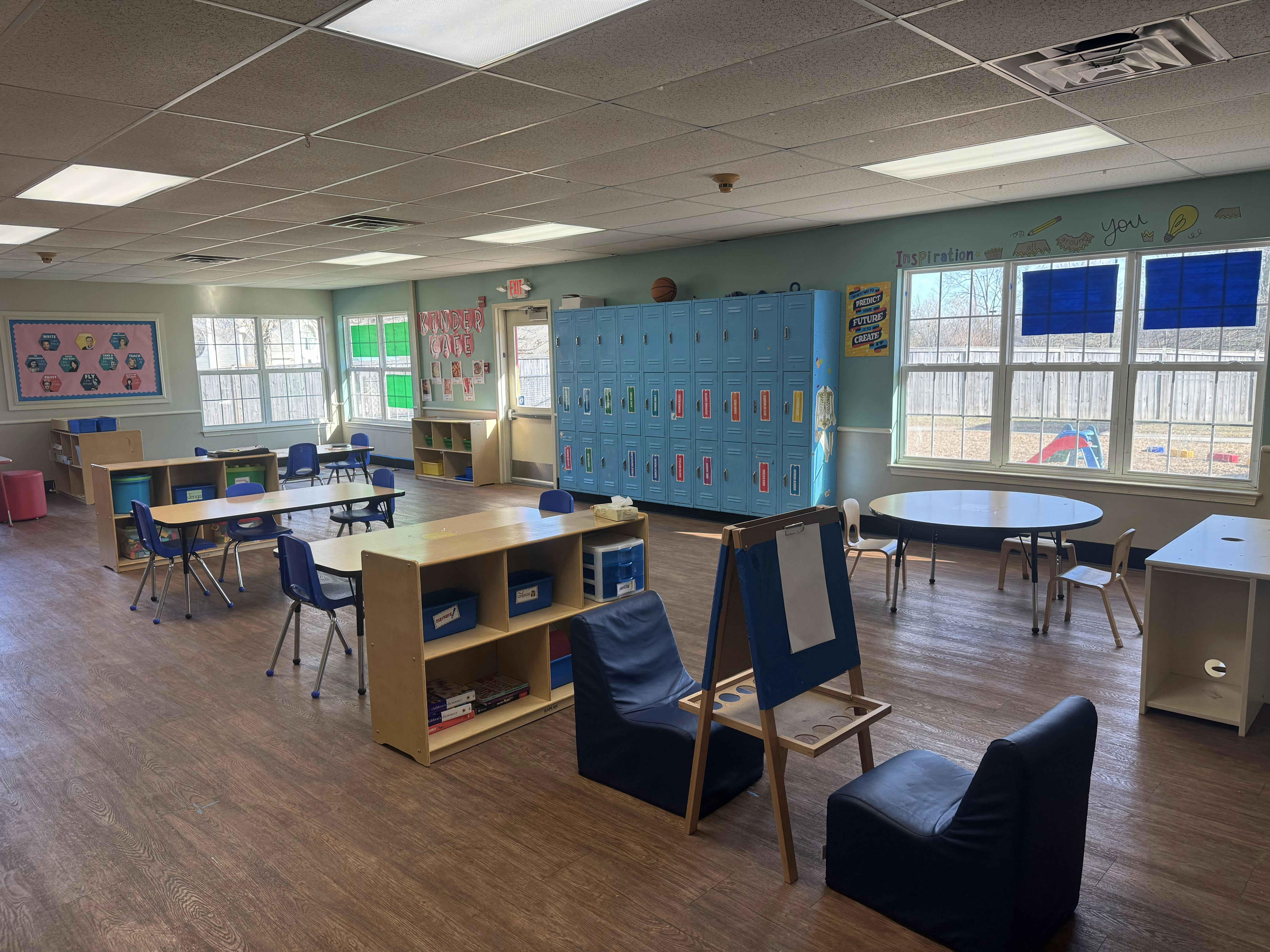 Classroom with small tables, chairs, blue lockers, and windows looking outside