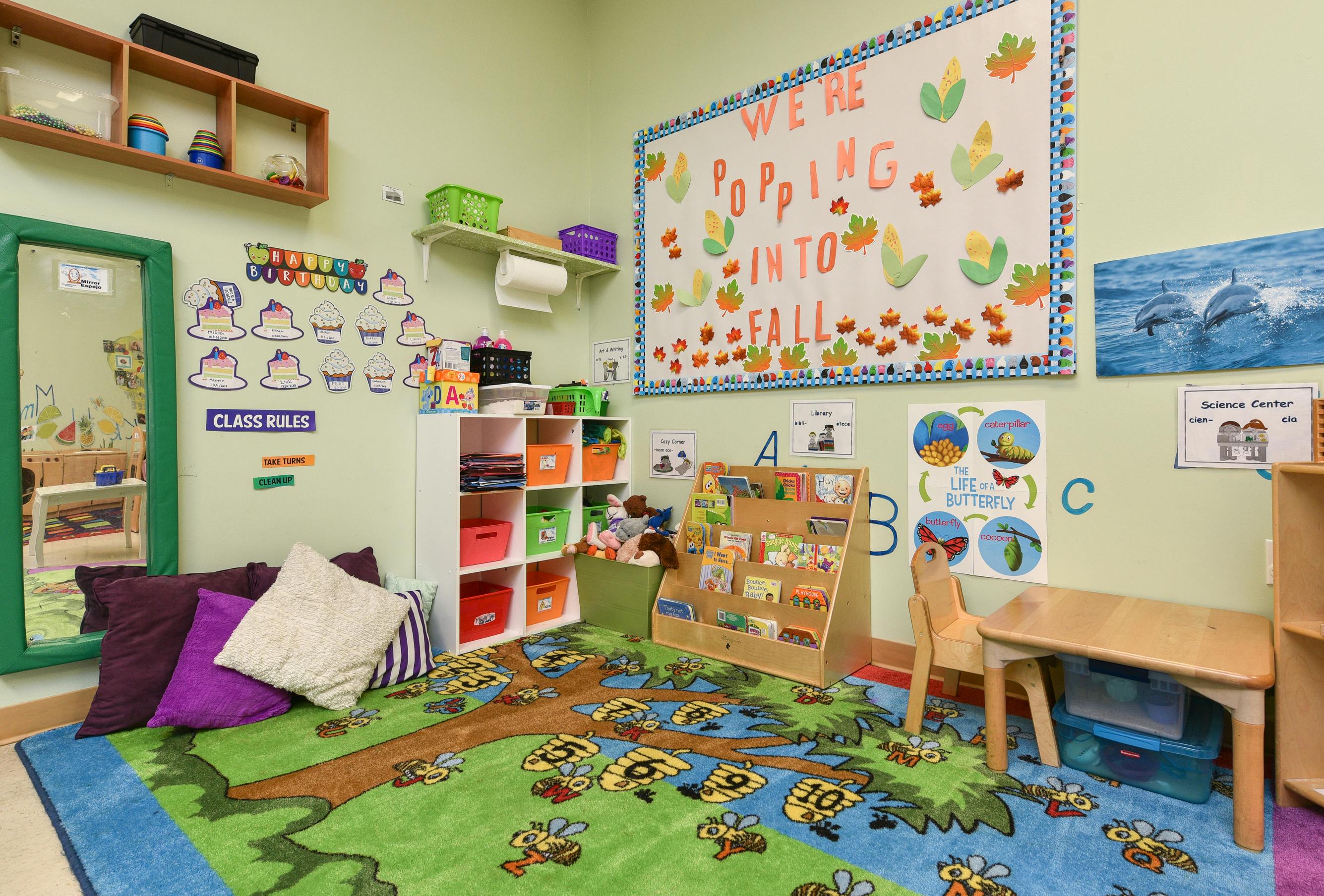 A colorful classroom with a rug, shelves, and a whiteboard that says "We're Popping into Fall"