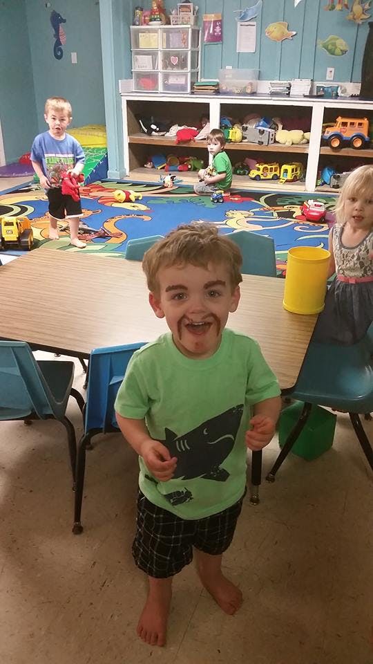 Child with drawn-on mustache and eyebrows in a classroom