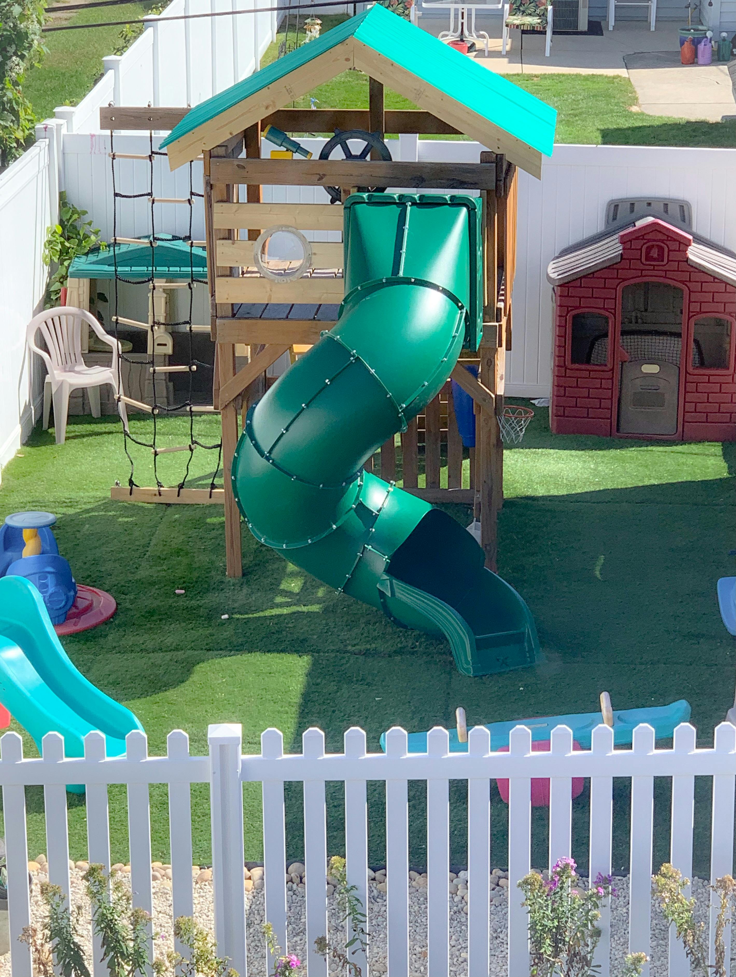 Playground with a green slide, climbing net, and a small red playhouse