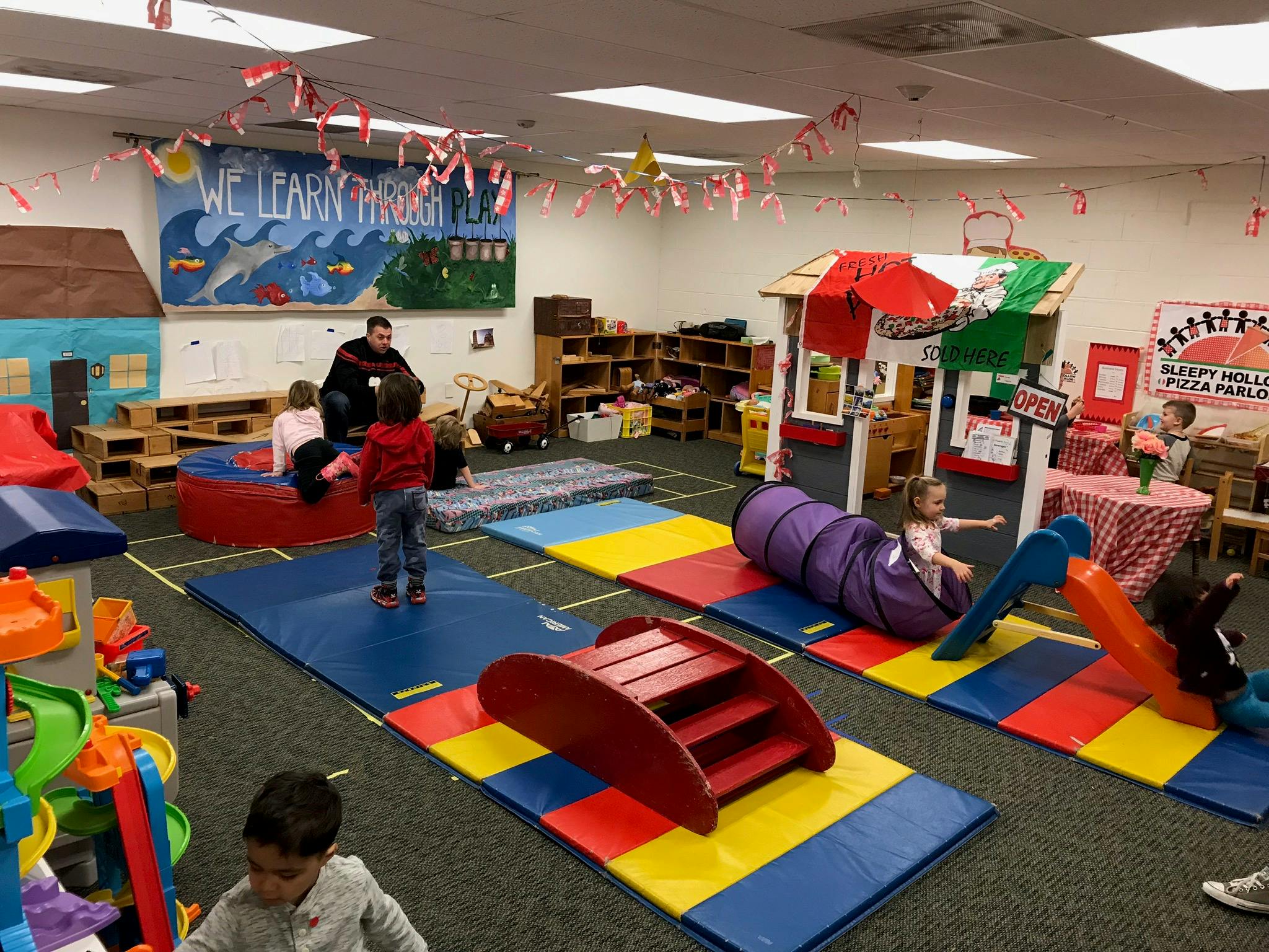 Children playing in a colorful indoor play area with mats and tunnels