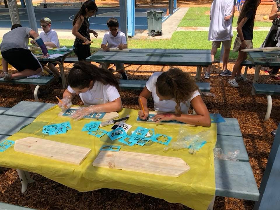 Two people working on crafts at a picnic table outdoors