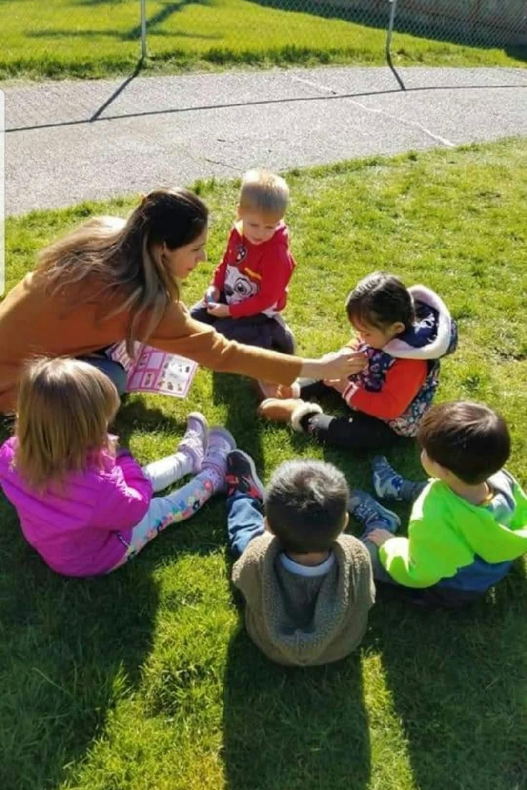 Person interacting with children sitting on grass