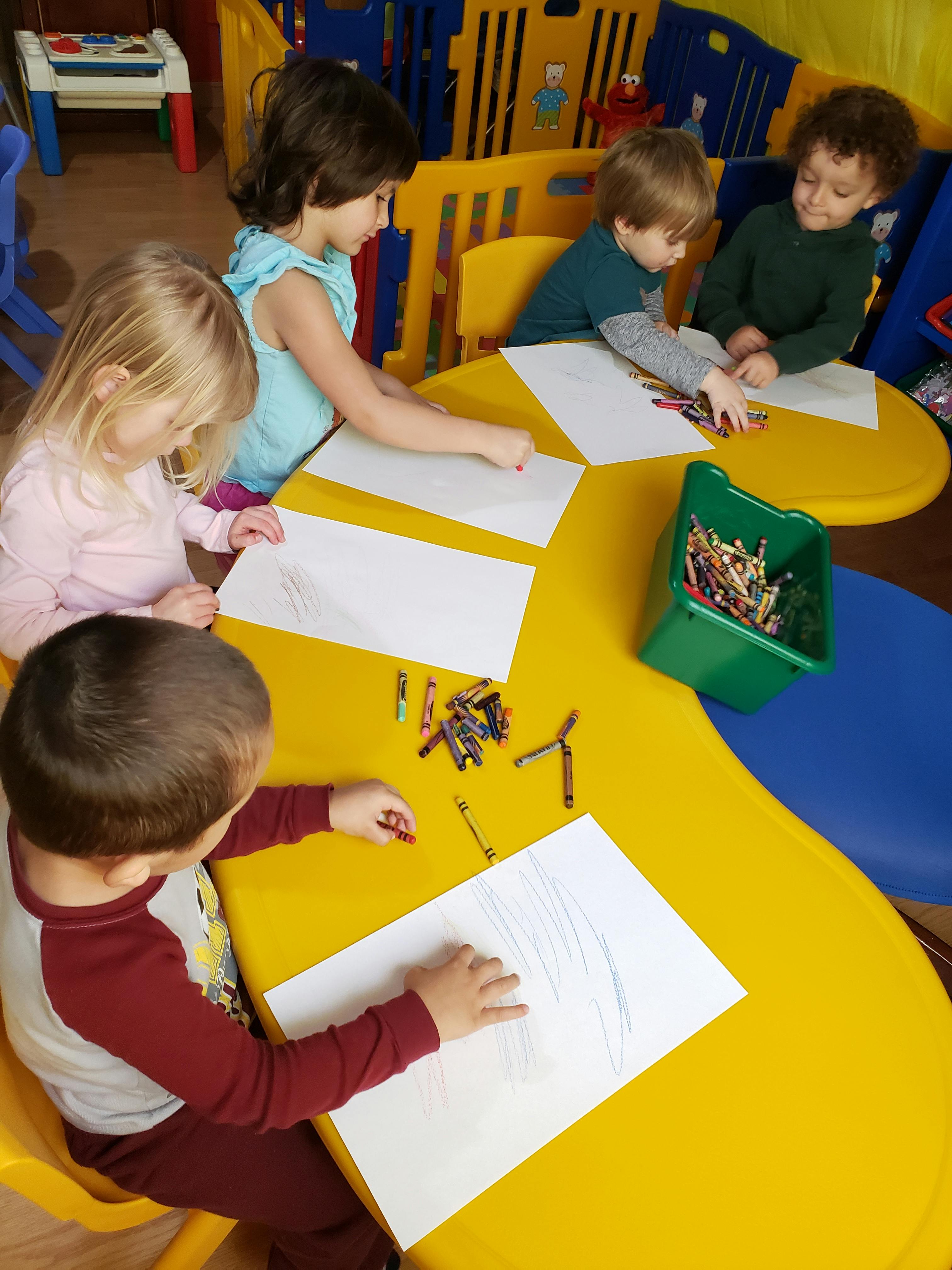 Children drawing with crayons at a yellow table