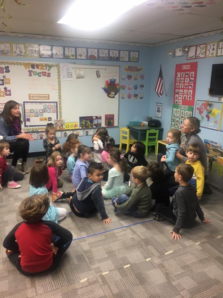 Adults and children sitting on the floor in a classroom
