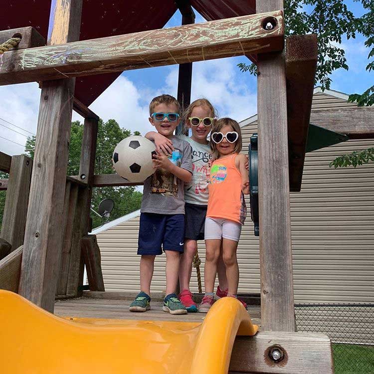 Three children with sunglasses on a playground, one holding a soccer ball