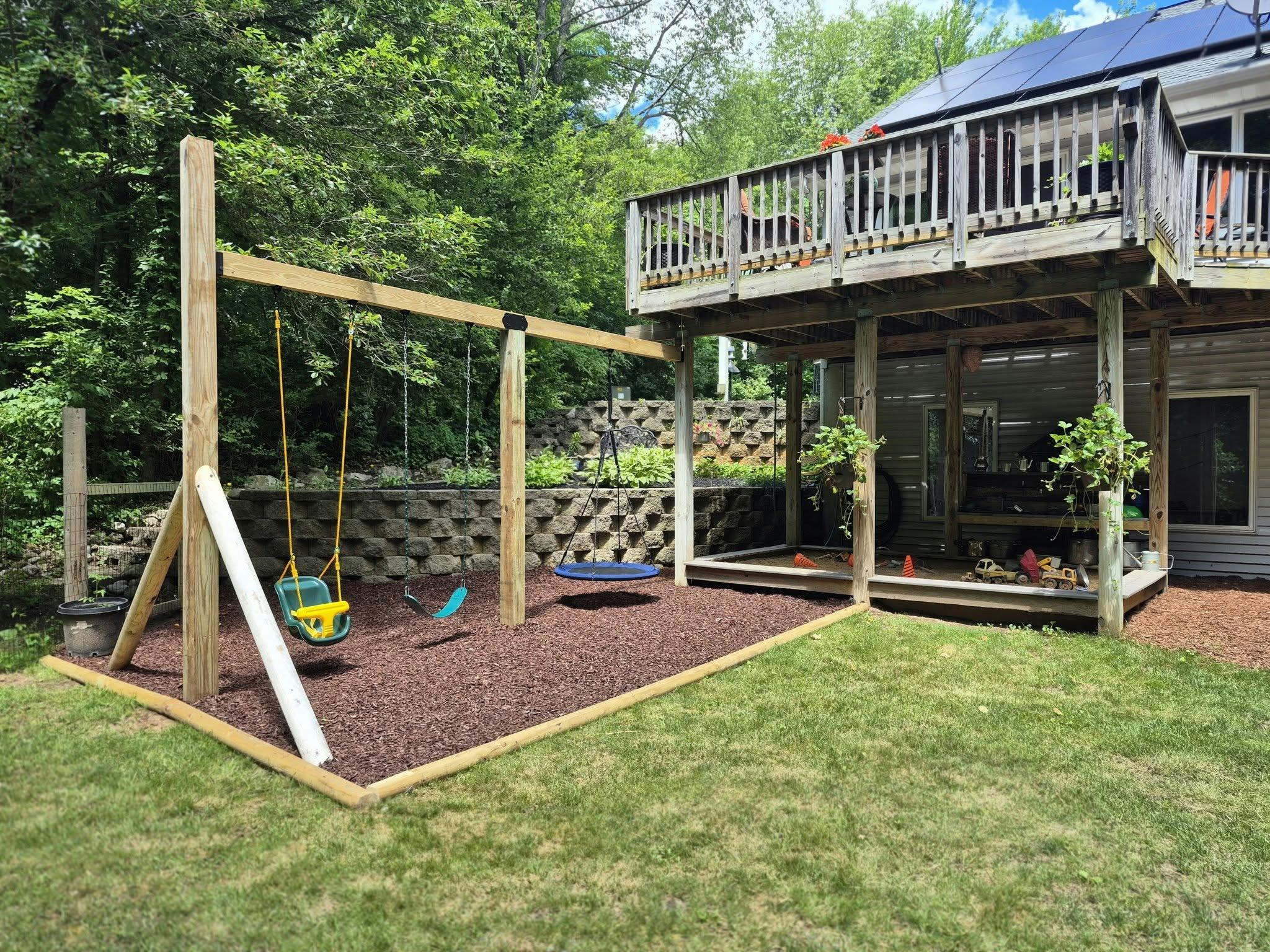 Backyard wooden swing set and sandbox beneath a wooden deck