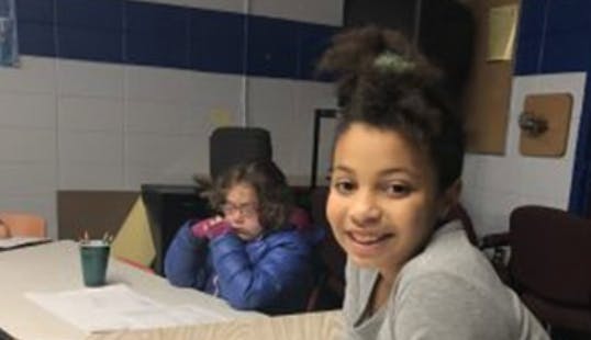 Child smiling at a table with another child in the background