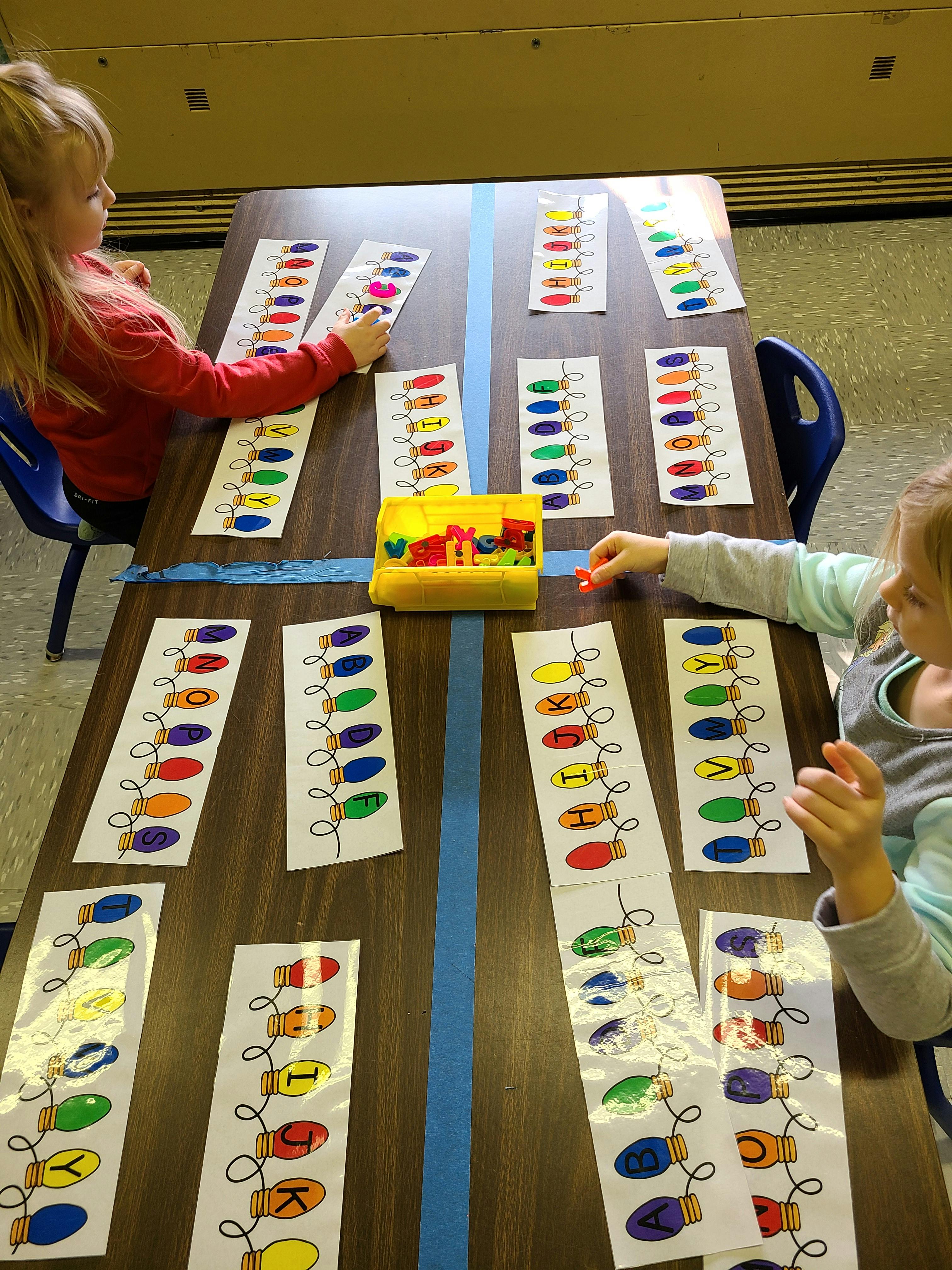 Two children playing with colorful light bulb cutouts on a table
