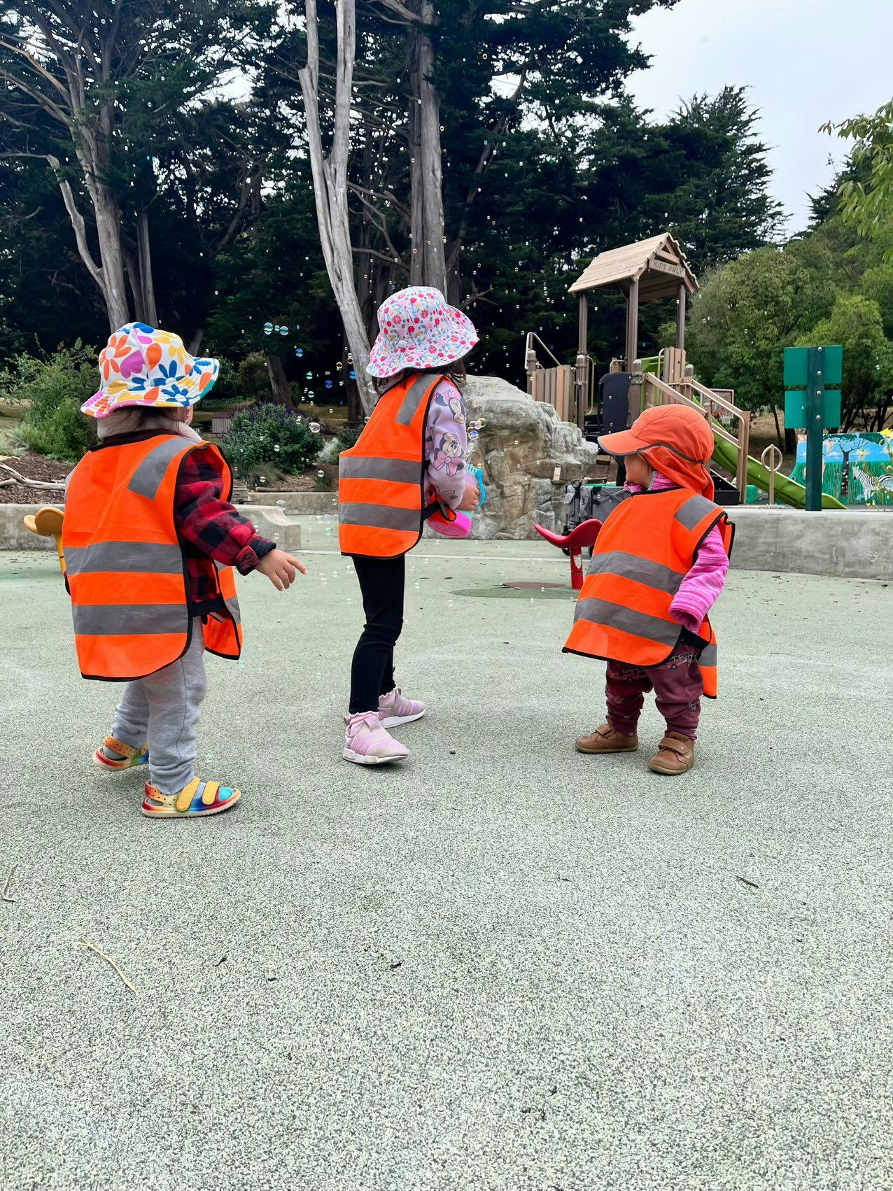 Three children in orange safety vests and hats playing outdoors