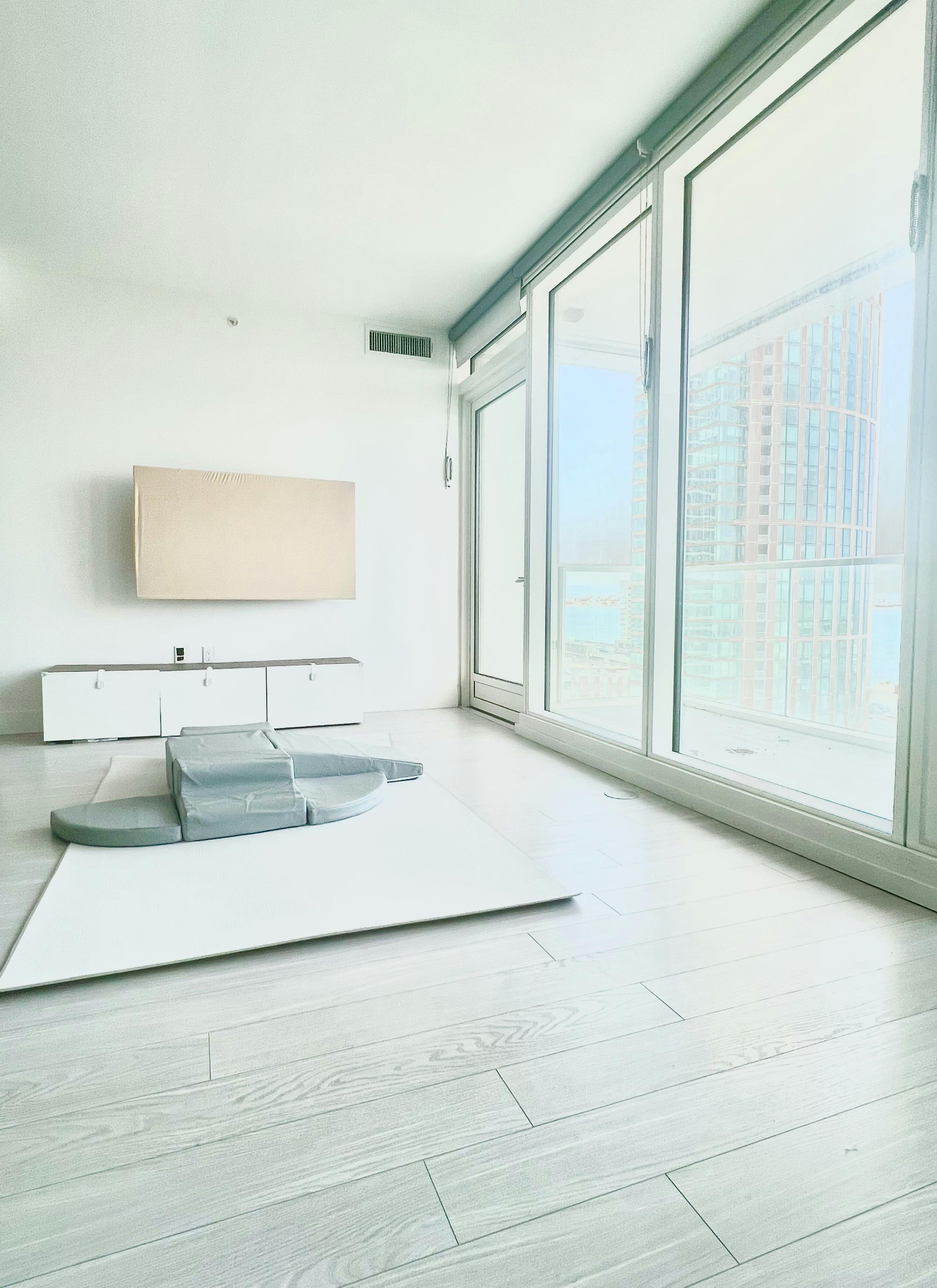 Empty room with large windows, a wall-mounted TV, and a play mat on the floor