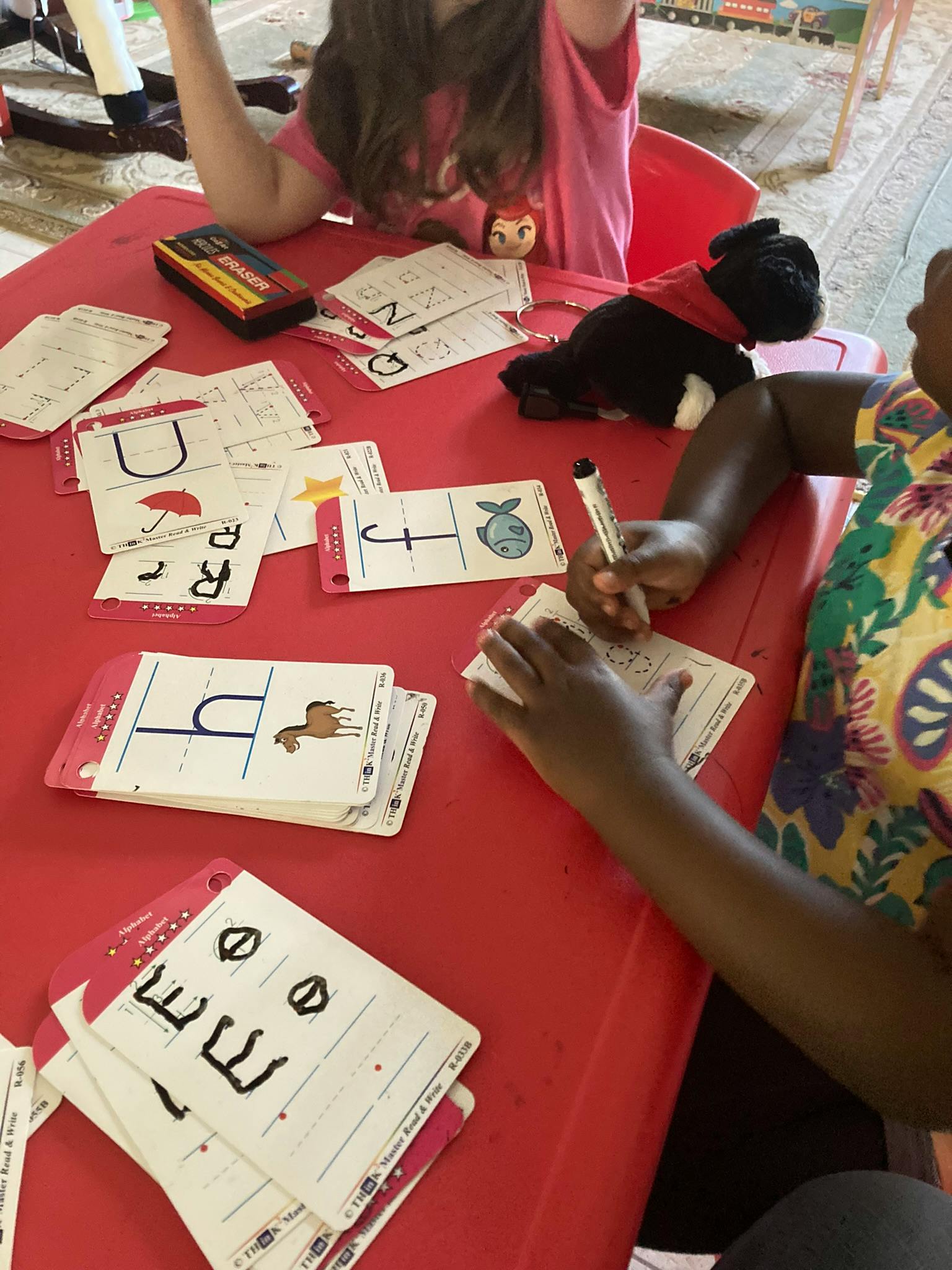 Child writing on a card at a red table with other learning cards
