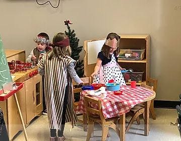 Three children playing in a classroom with a toy kitchen and table
