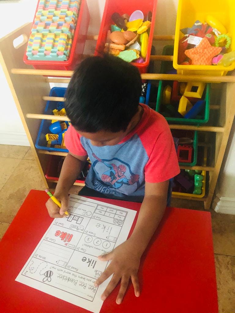 Child writing on a worksheet with a pencil at a red table