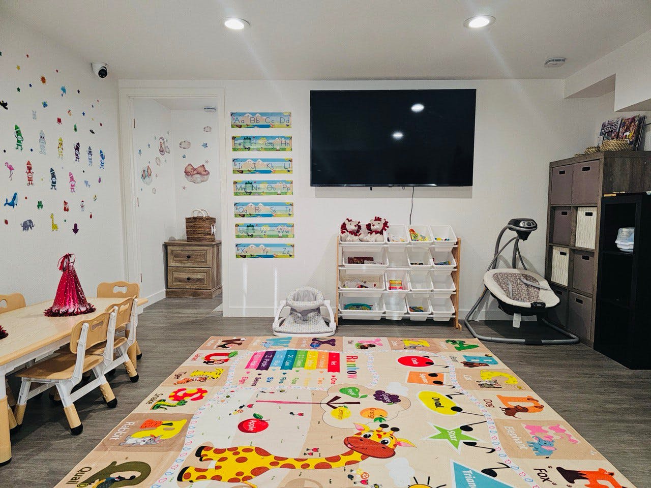 Playroom with a colorful alphabet mat, small table and chairs, and a television