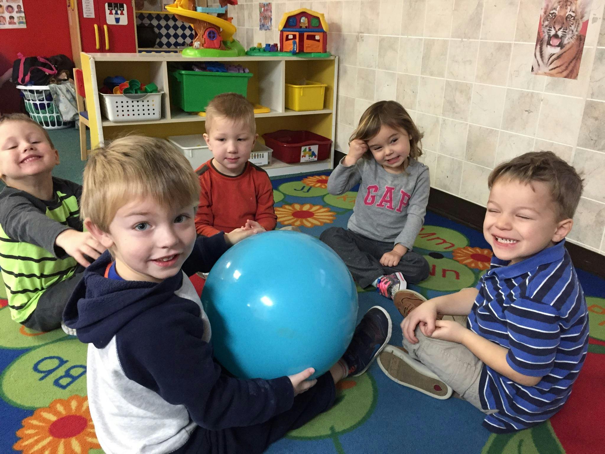 Five children sitting on a colorful rug with a blue ball