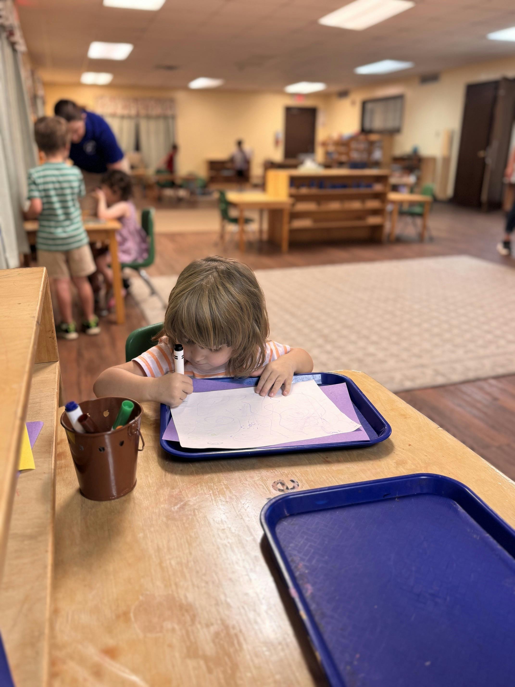 Child drawing on paper at a table in a classroom
