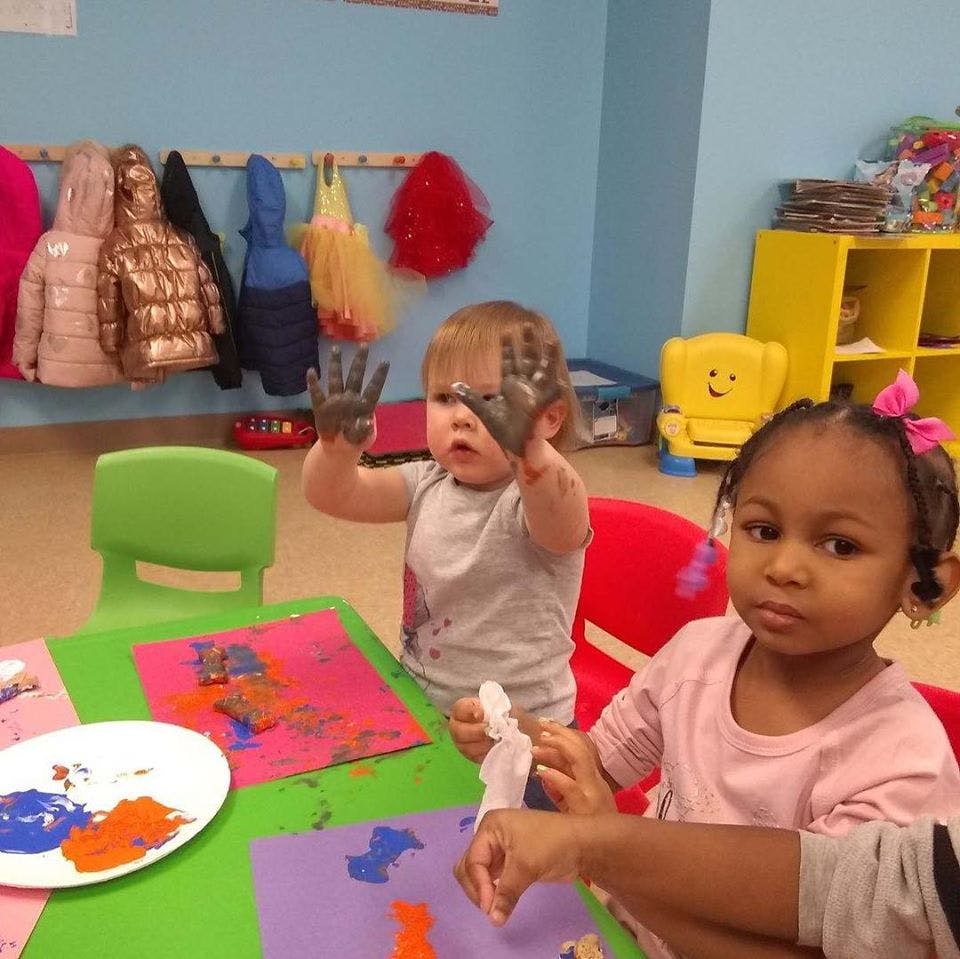 Two children painting at a table, one with paint on hands
