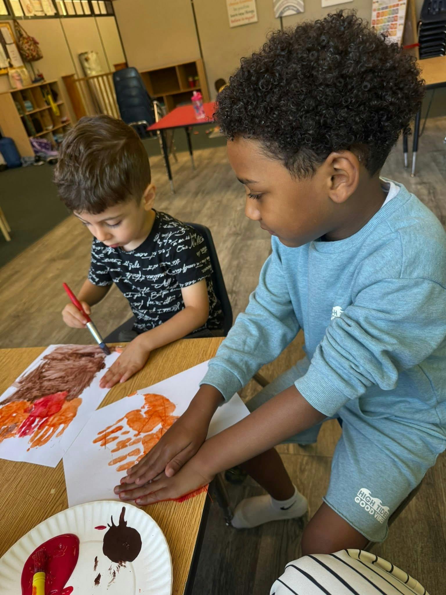 Two children painting with their hands and paintbrushes at a table