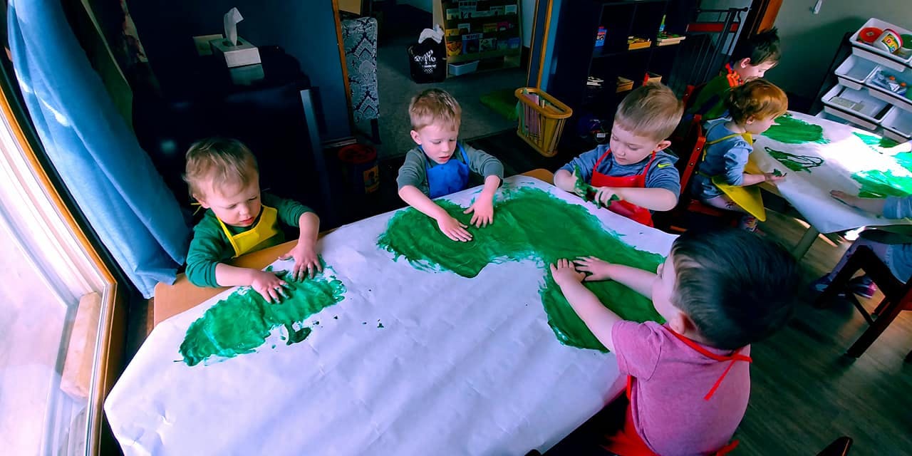 Children finger painting with green paint on a large white sheet