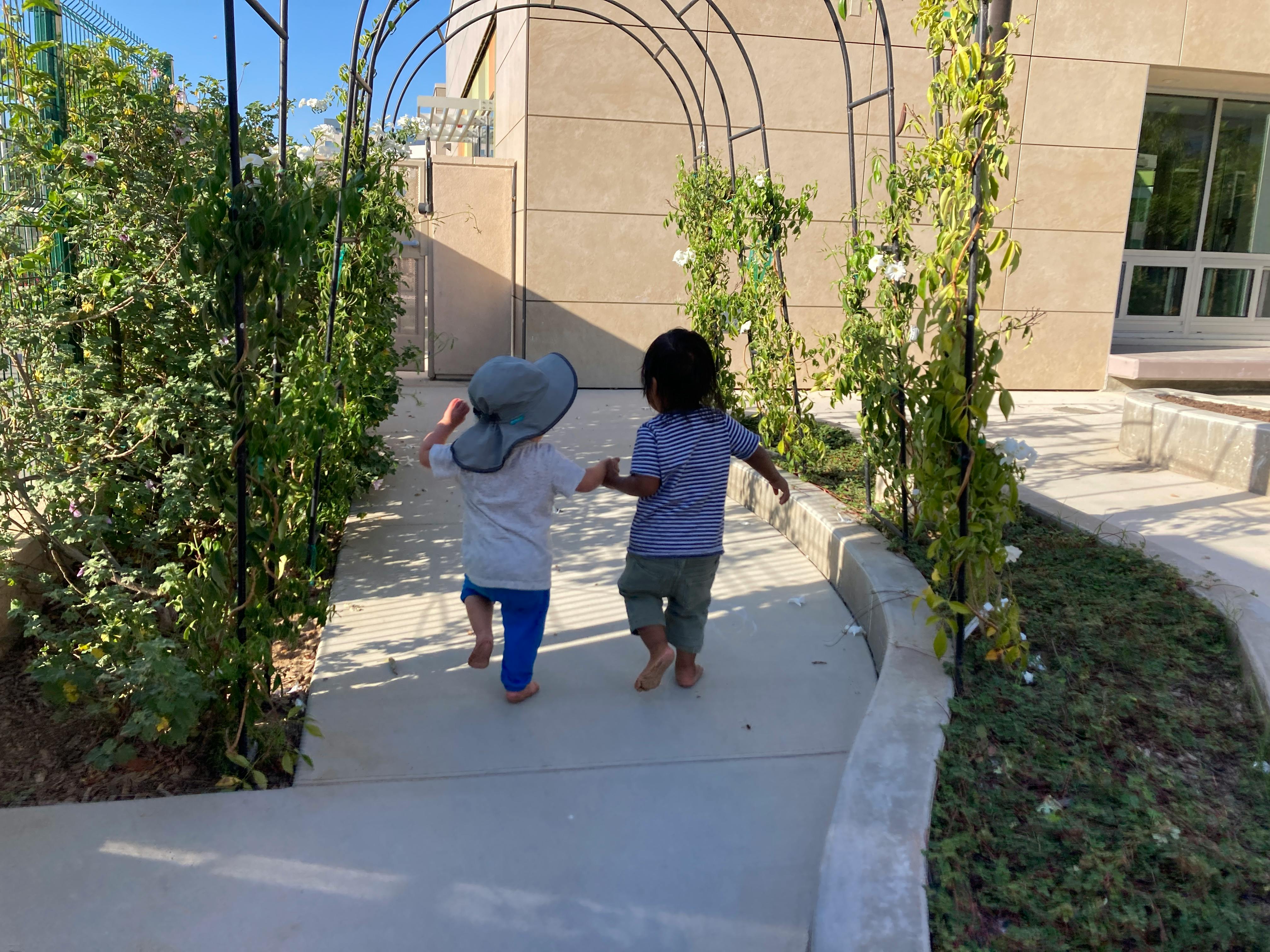 Two children walking on a path under an archway of plants