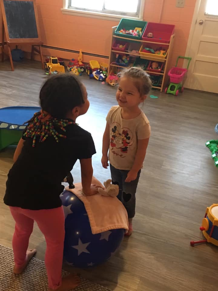 Two children playing with a large blue ball in a room with toys