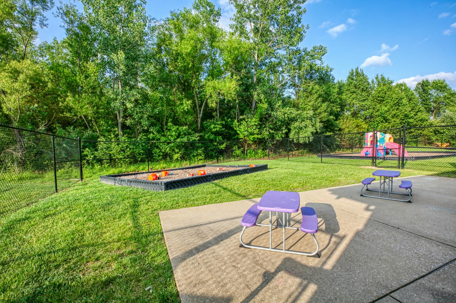 Purple picnic tables on a concrete patio next to a sandbox and playground