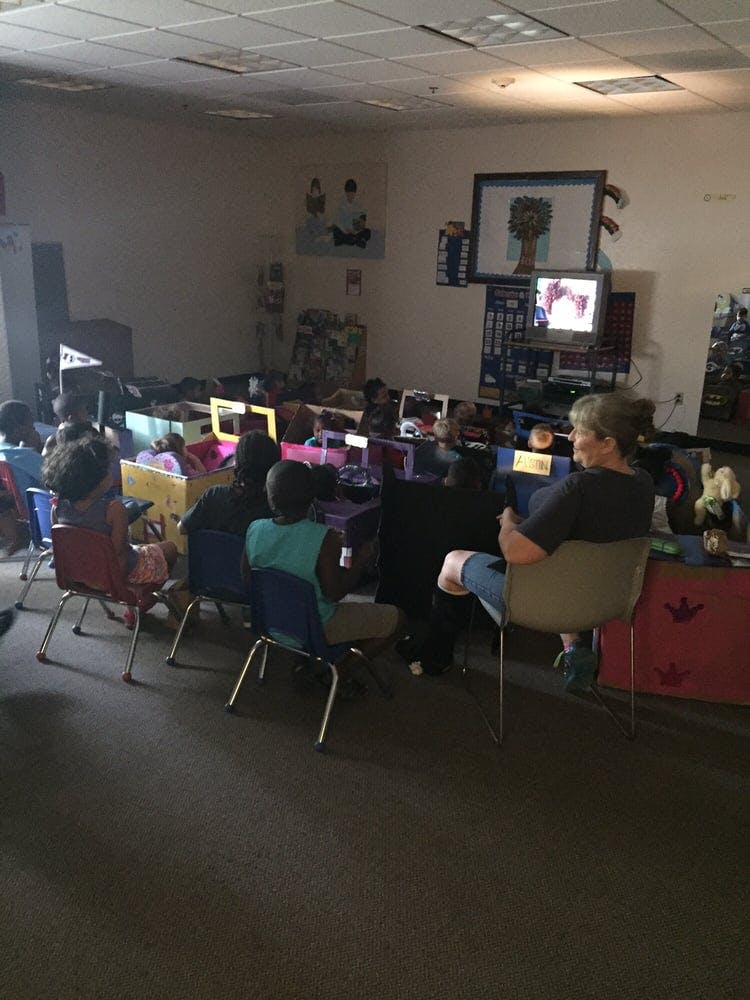 People and children sitting in a room watching a screen