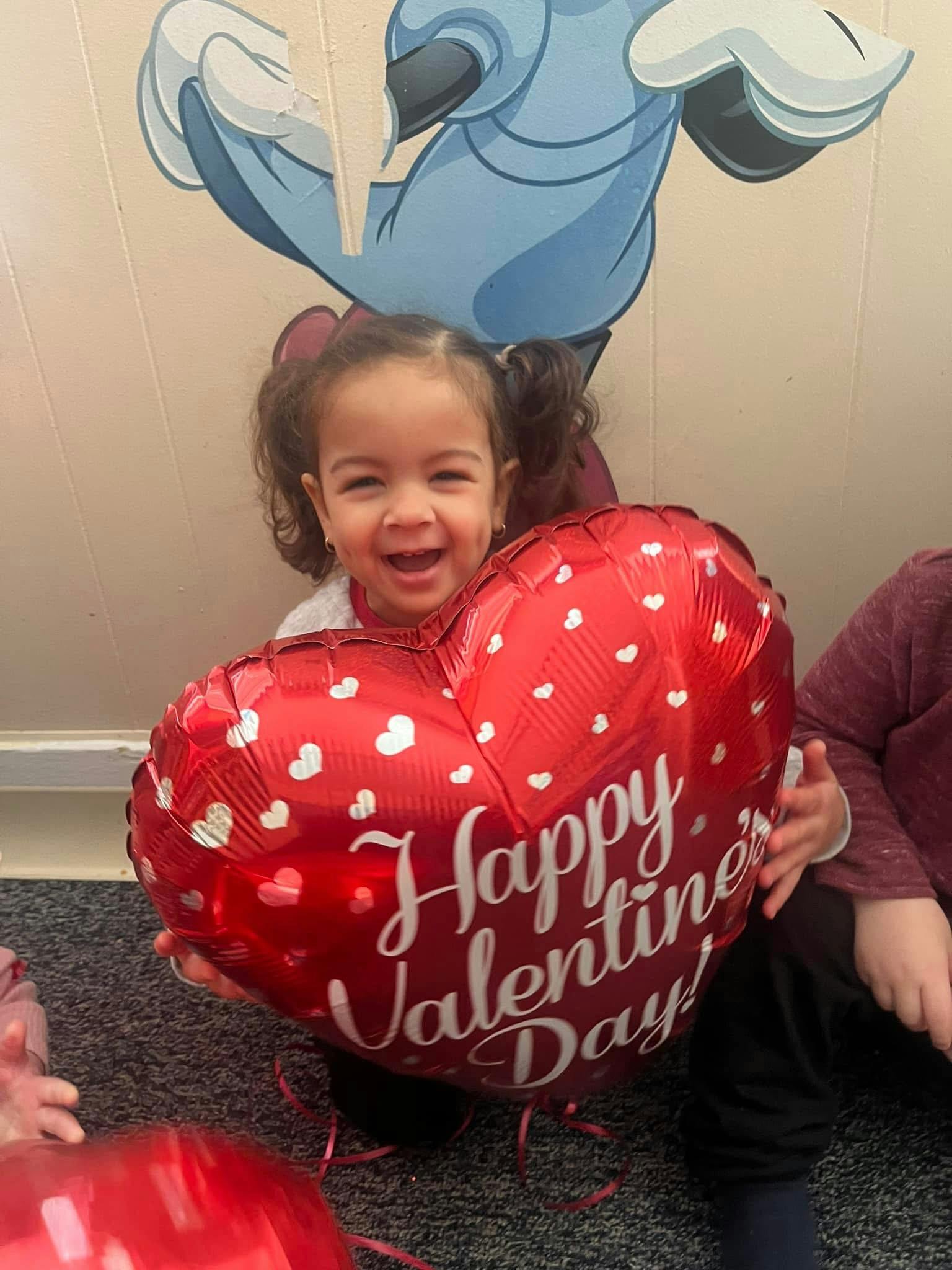 Child holding a red heart-shaped balloon that says "Happy Valentine's Day"