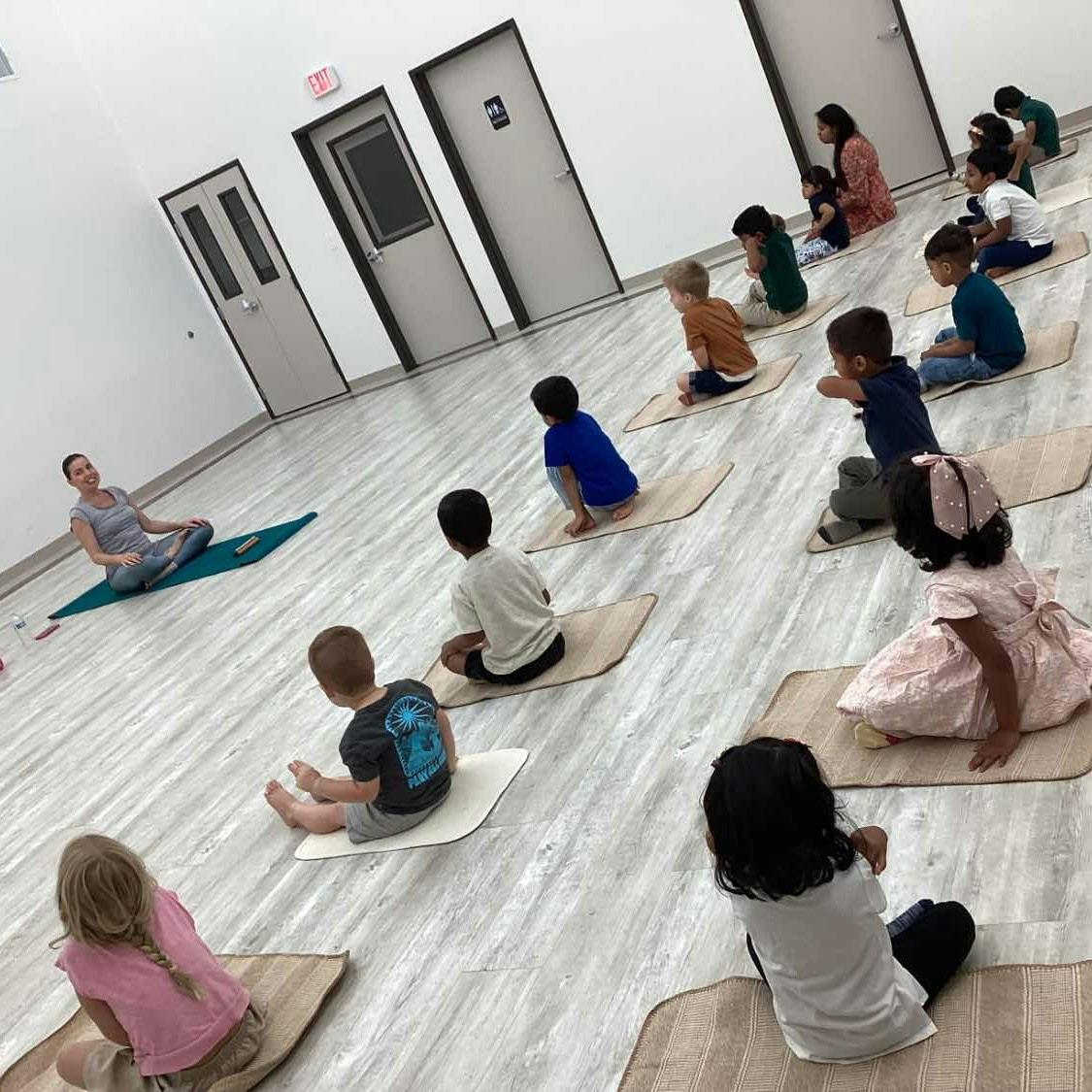 Adult and multiple children sitting on mats in a room