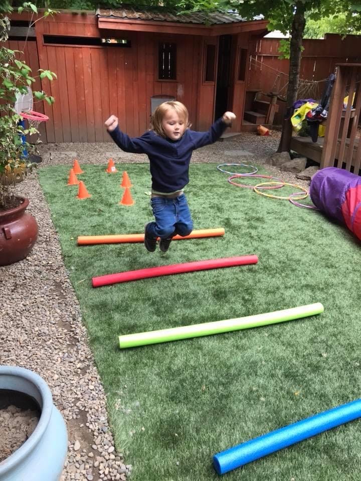 Child jumping over colorful foam noodles on artificial grass