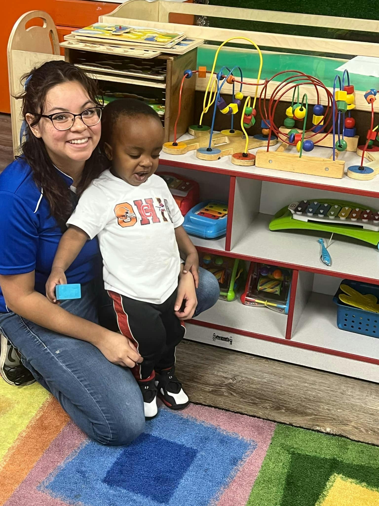 Smiling person kneeling next to a child in a classroom