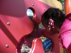 Child looking through a hole in a red playground structure