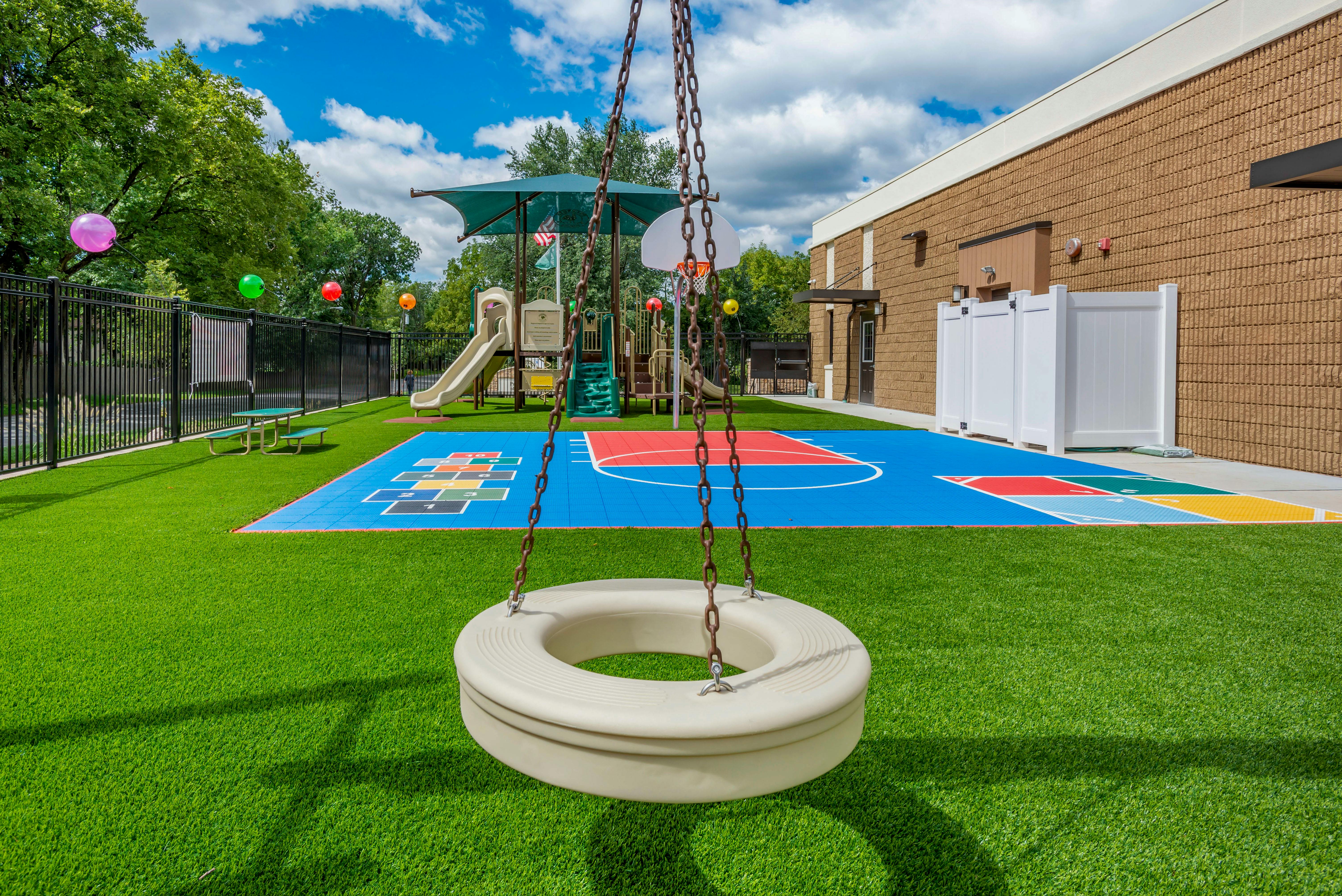 An empty playground with a tire swing in the foreground, slides, and colorful court