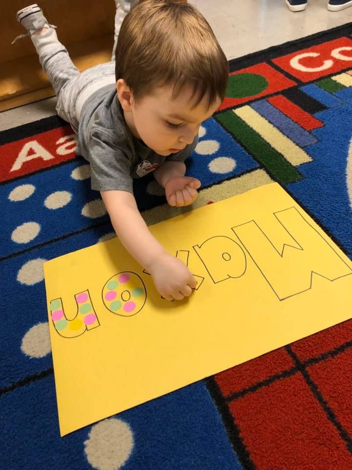 Child on floor decorating a yellow sign with the word "Max"