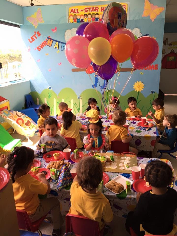 Children sitting at tables with food and balloons in a classroom