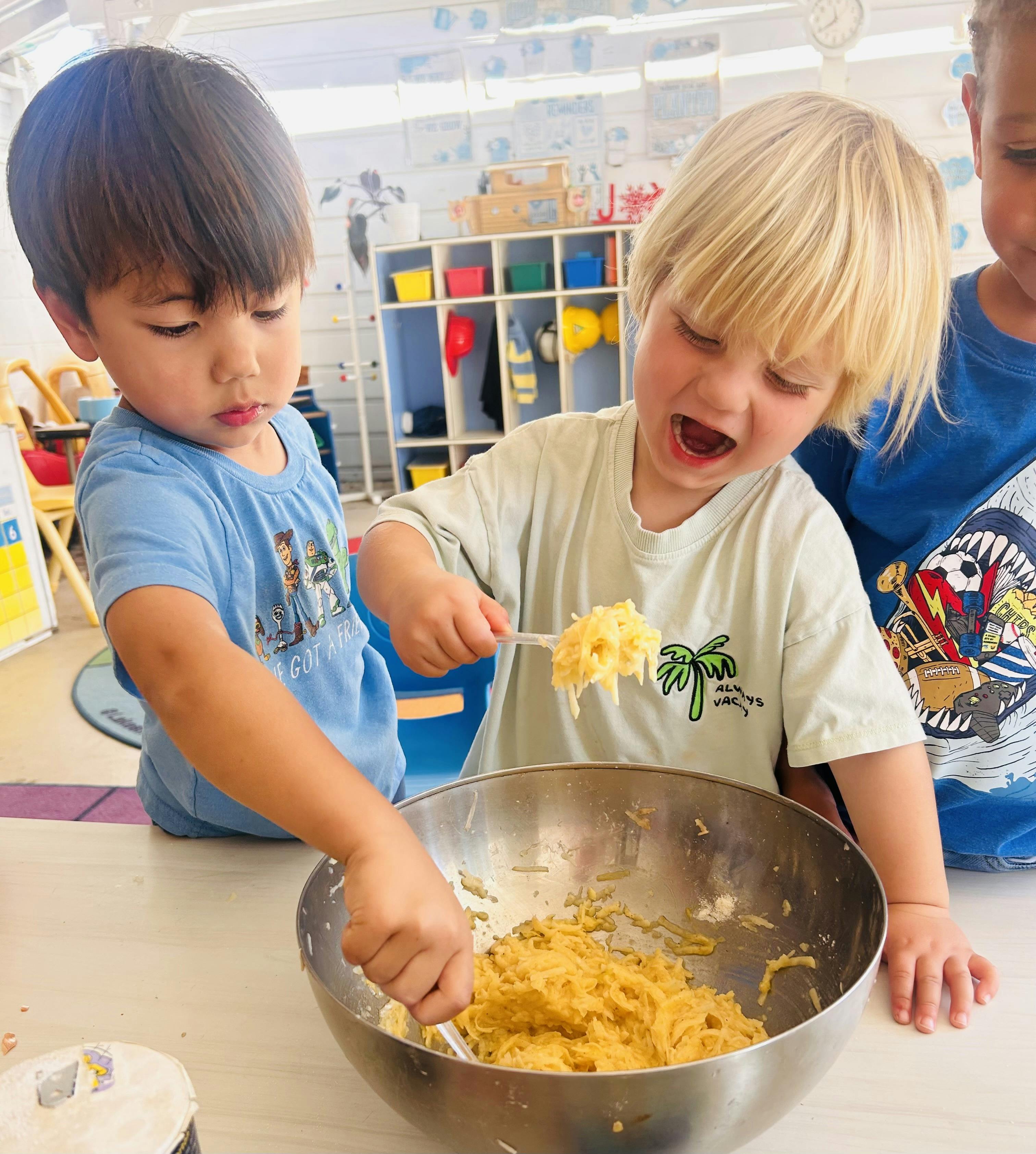 Three children mixing contents in a metal bowl with spoons