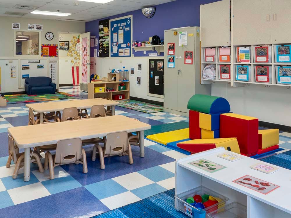 A colorful empty classroom with small tables and chairs, and soft play equipment