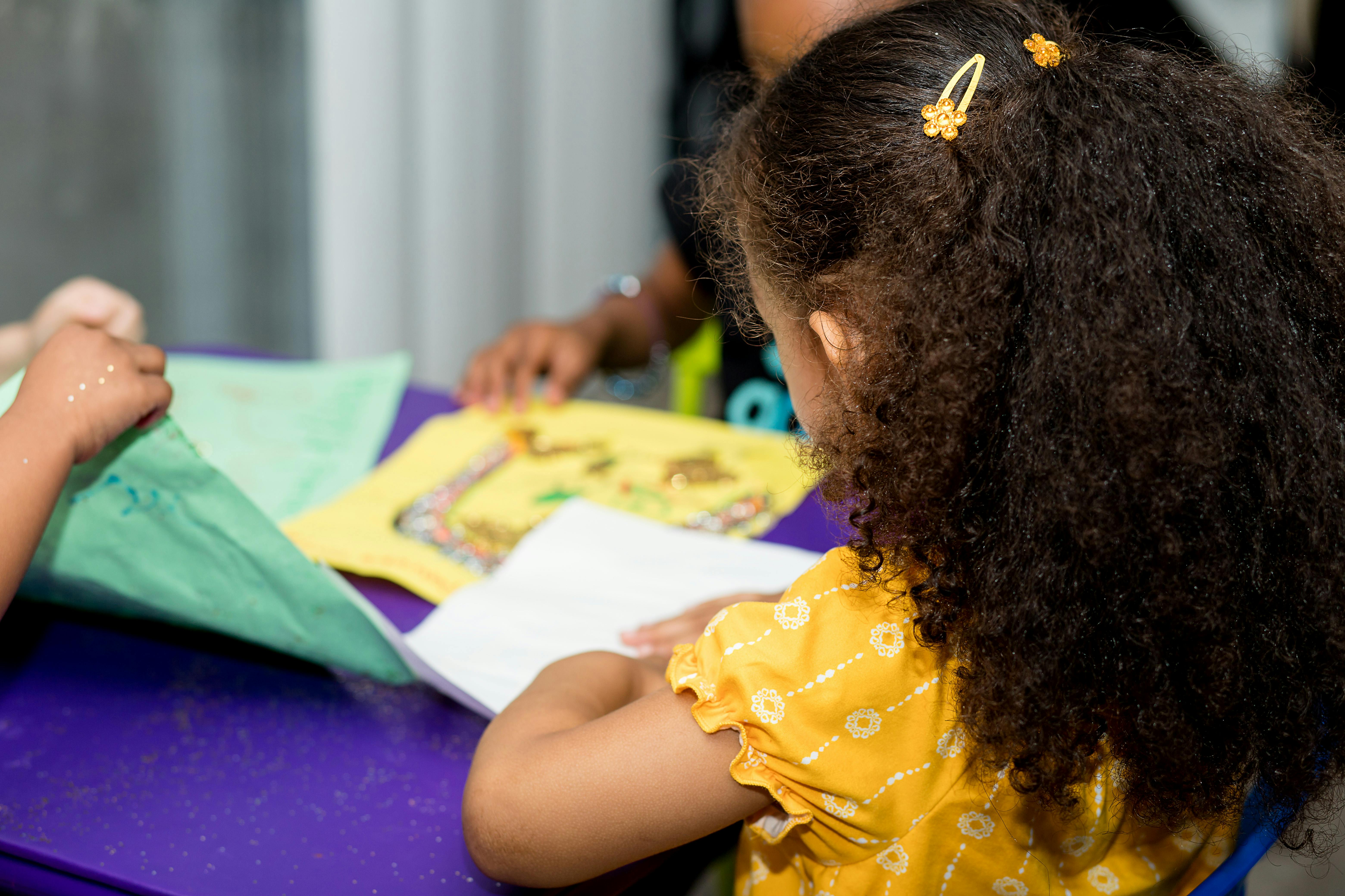Child with curly hair looking at a book at a table