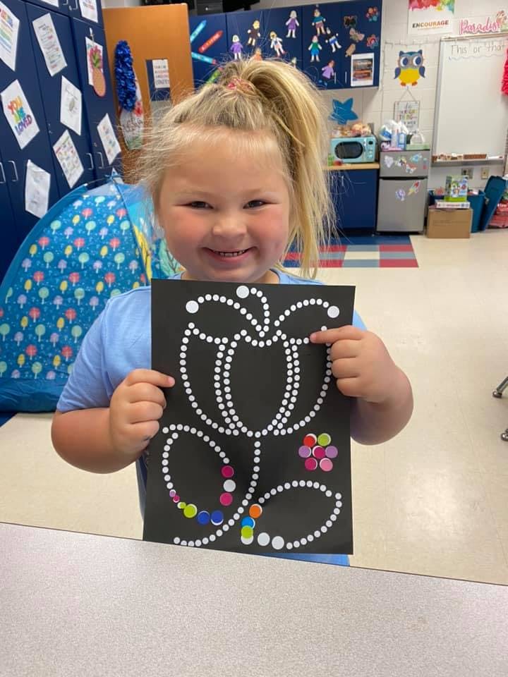 Child holding up a black paper with a white dotted butterfly design