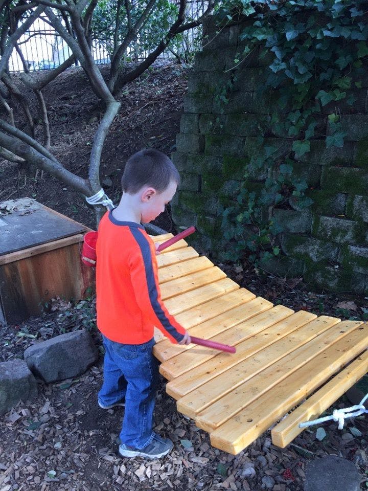 Child playing a large wooden xylophone outdoors