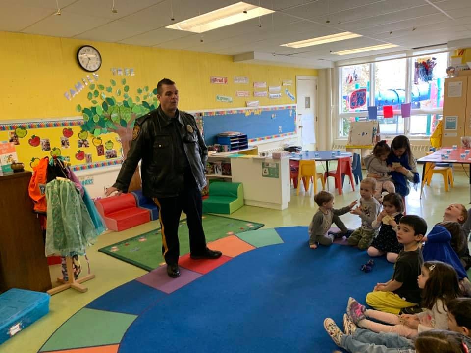 Person in uniform speaking to children seated on a rug in a classroom