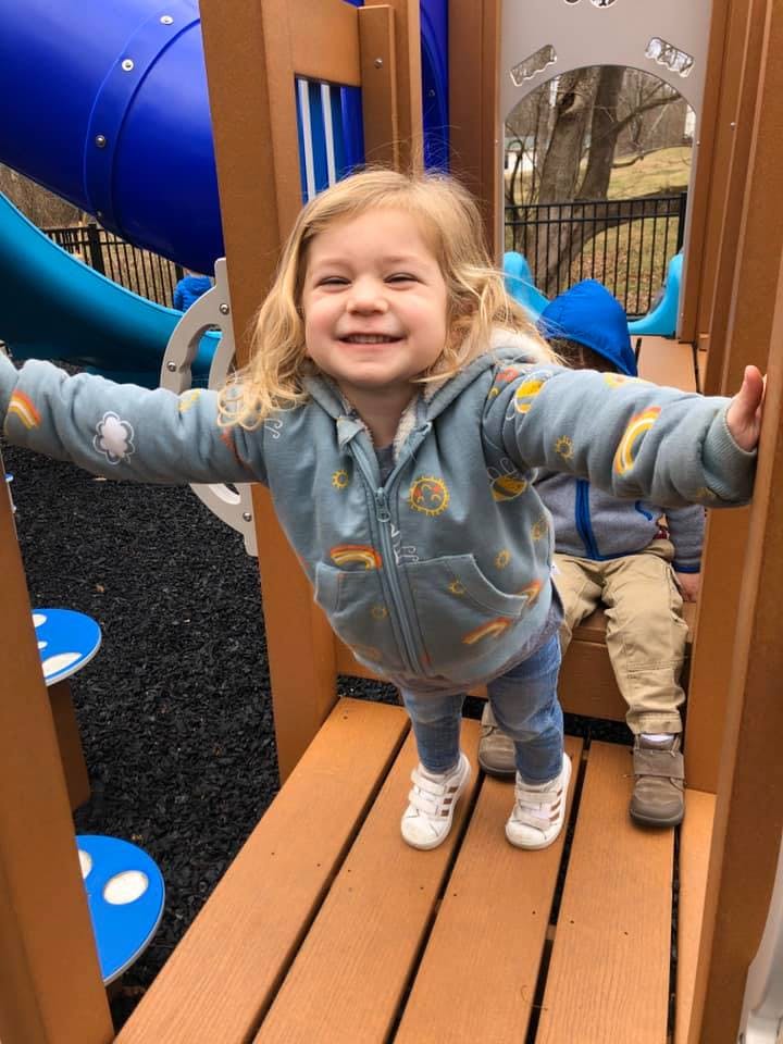 Child standing on a playground structure with arms outstretched