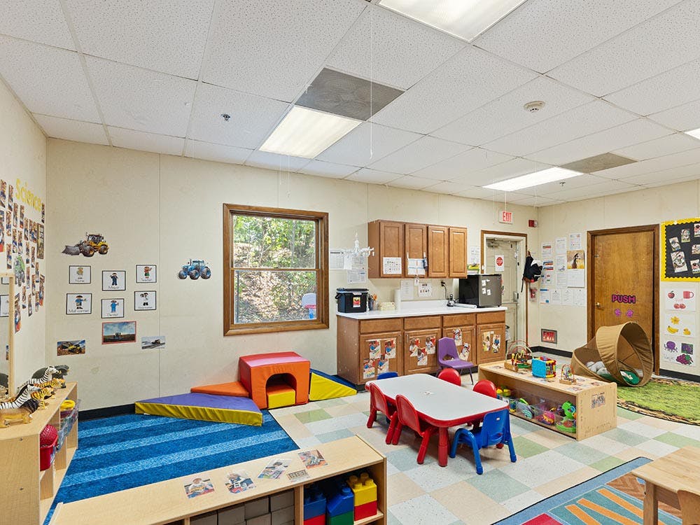 Childcare classroom with colorful rugs, tables, chairs, and play equipment