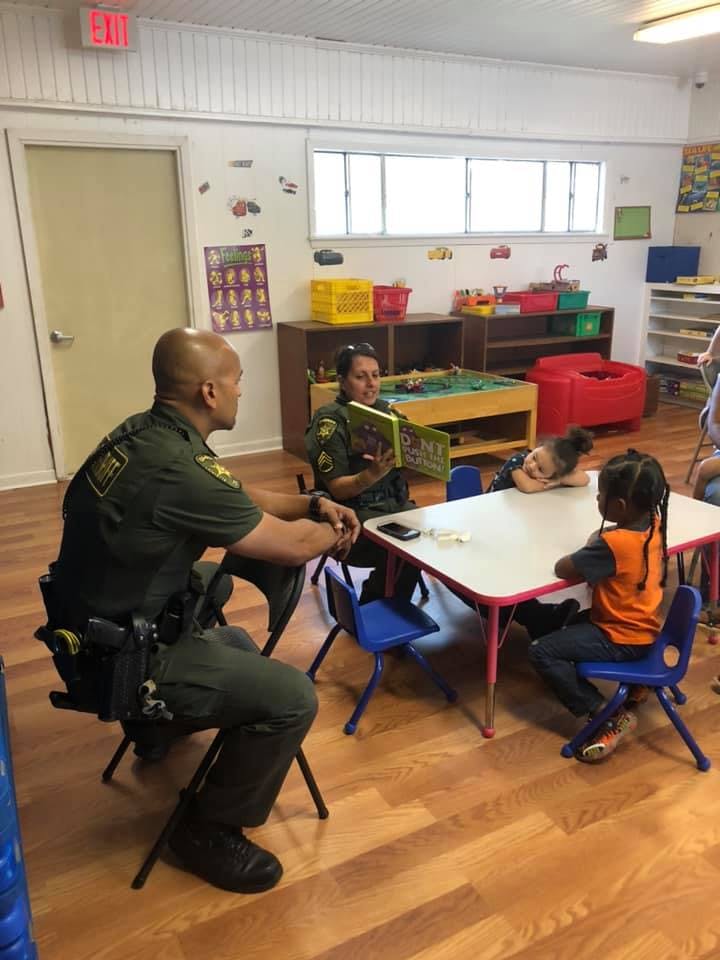 Two people in uniform reading to children in a classroom